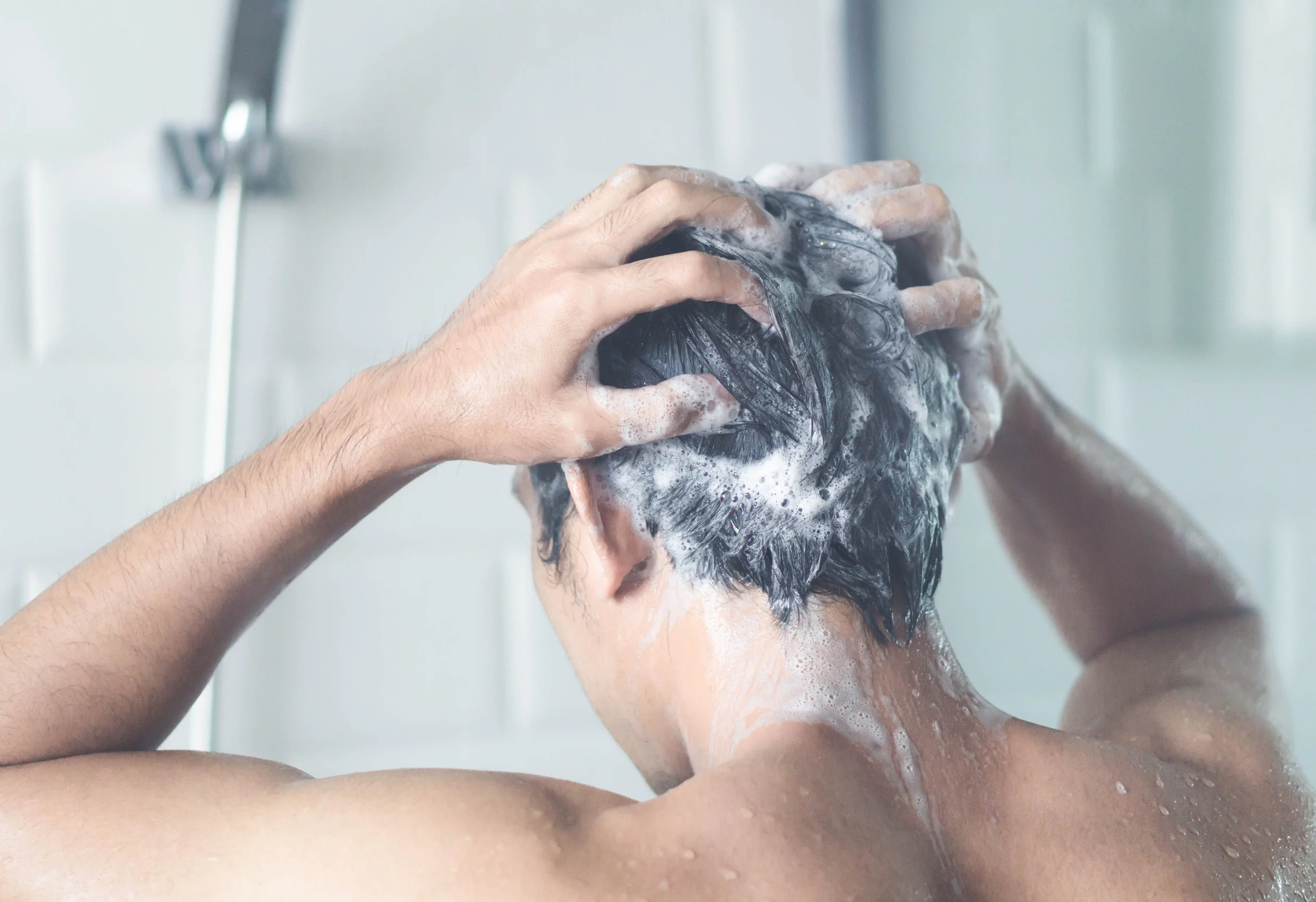 Un uomo che si massaggia i capelli durante lo shampo, per infoltire i propri capelli.